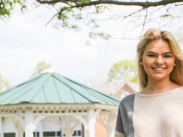 Caitlyn stands near a gazebo on campus.