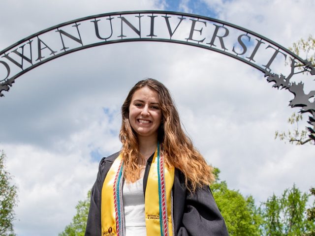 Alyssa smiles and stands in front of the Rowan arch.