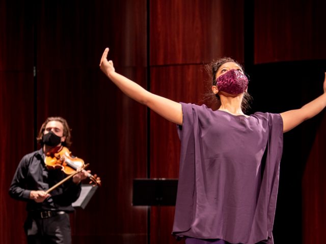 Amanda dancing on stage in a purple outfit and mask with the ensemble around her.