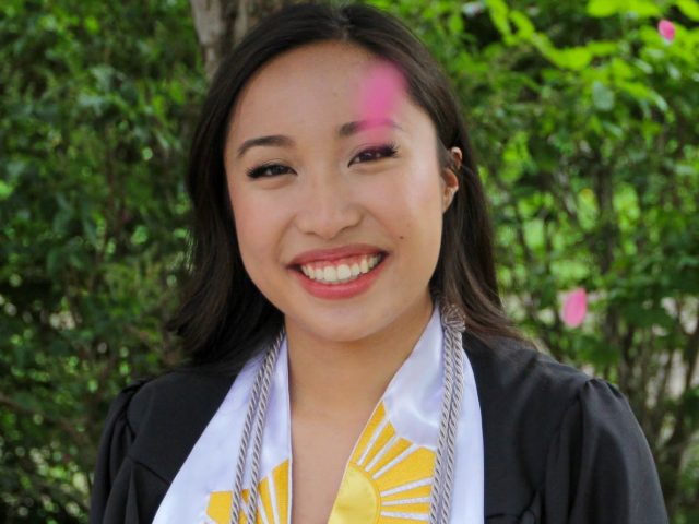 Marian poses in front of a bush with her graduation regalia.