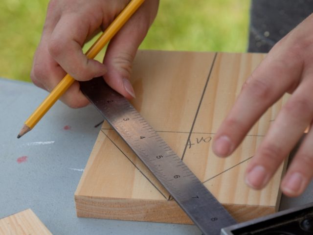 Someone measures a line on a piece of wood.