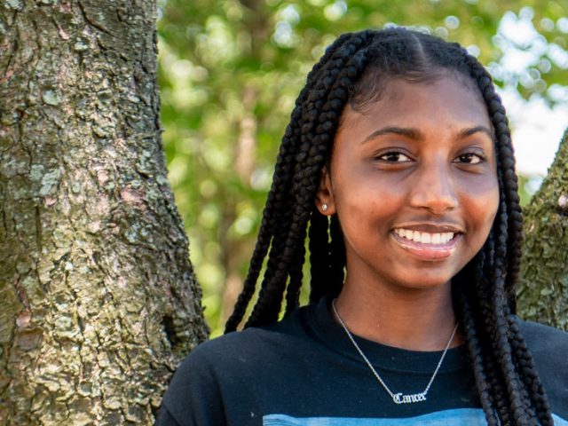 Nene smiles in front of a tree on campus.