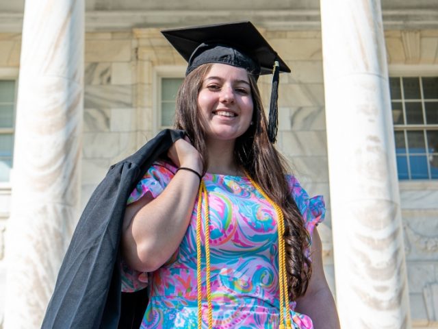 Kassidy stands in front of Bunce Hall with her cap and gown.