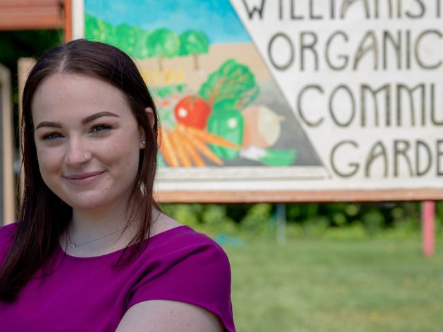 Jenna stands by the entrance sign for the Williamstown Organic Community Garden.