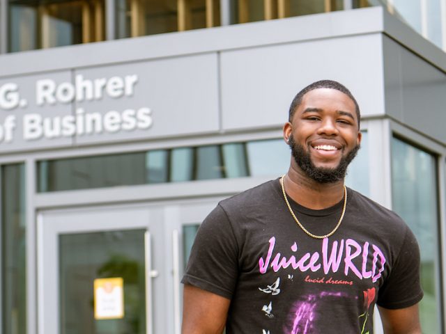 Reshaun smiles and stands in front of the entrance to Business Hall.