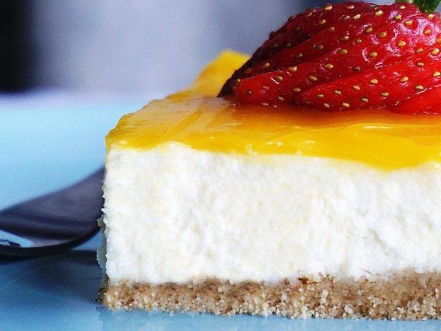 Close up of a slice of white cheesecake with lemon yellow glaze and a strawberry.