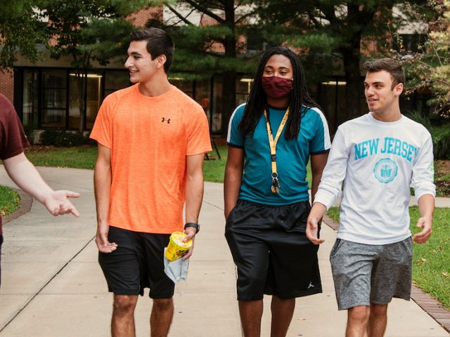 Five students walk and talk on campus.