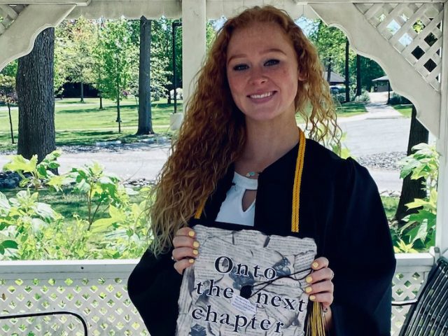 Chloe holds her decorated cap inside a gazebo on campus.