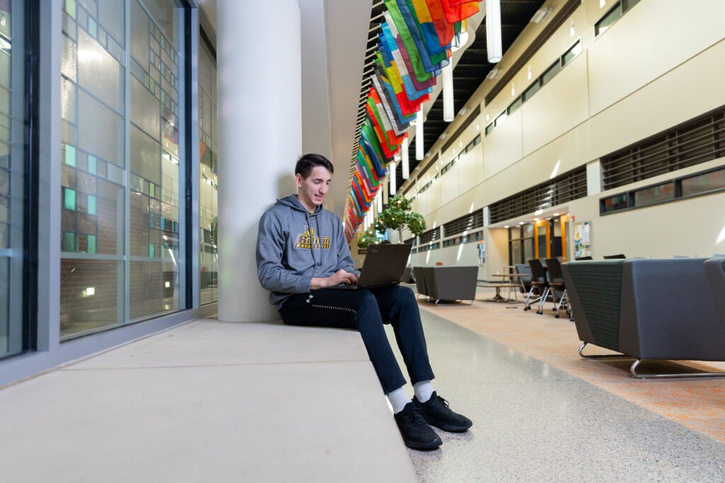 A student studies on his laptop sitting on a concrete sitting platform within James Hall.