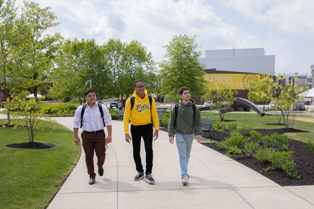 3 students walking with a Rowan sign behind them