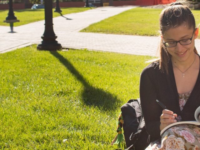 Brianna journals on the lawn next to the Campbell Library.