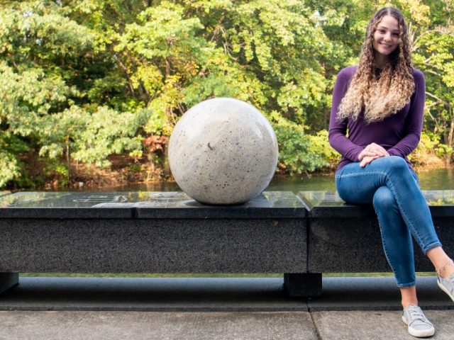 Lauren sits on a bench next to a white, sphere sculpture.