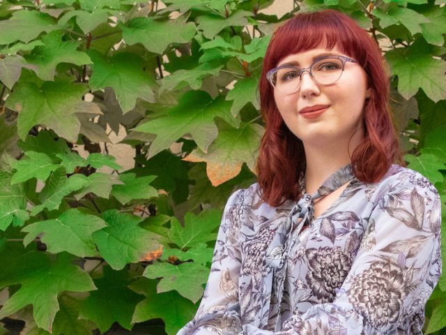 Rowan English graduate Nicole sits in front of fall foliage on campus.