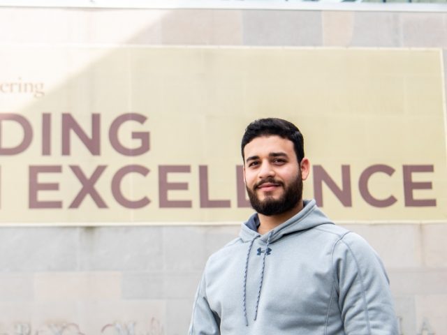 Omar stands in front of the banner at Rowan Hall.