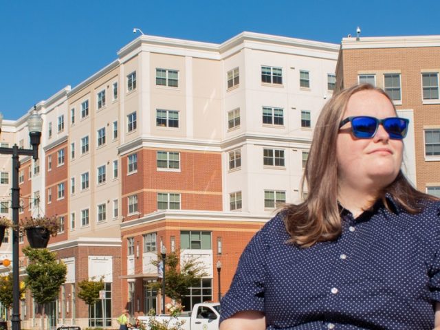 Carrie sits on Rowan Boulevard with the view of Rowan Boulevard behind her.