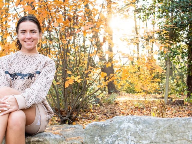 Trinity sits on a rock in front of trees.