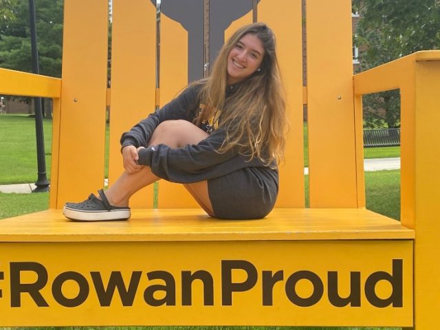 Valentina poses on the #RowanProud chair near Bunce Hall.