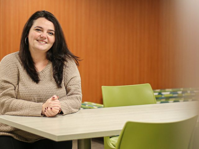 Catherine smiles and poses inside an academic building on campus.