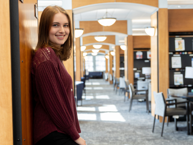 Jessica Newell smiles and stands inside the Chamberlain Library.