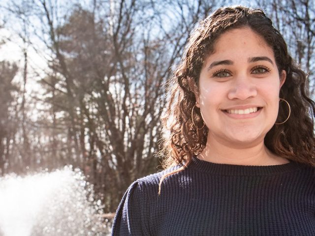 Maria is standing in front of a fountain smiling at the camera.