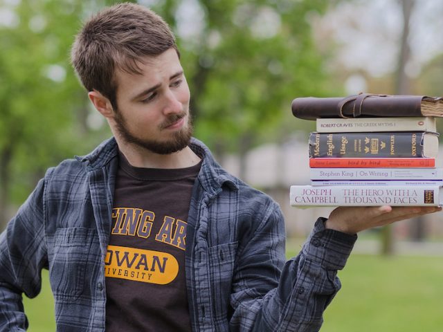 Eric Uhorchuk holds a stack of Writing Arts materials outside on campus.