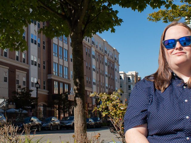 Carrie is sitting by the Rowan Boulevard with sunglasses on her face.