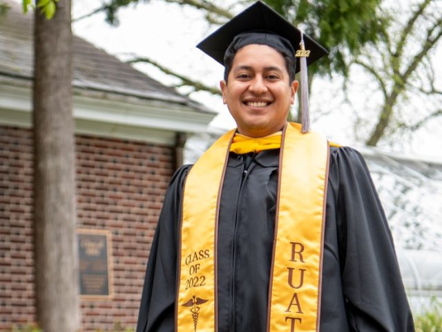 Marlon poses in front of a greenhouse in his graduation attire.