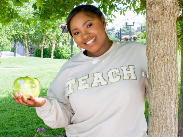 Mariah holds an apple while standing outside on campus.