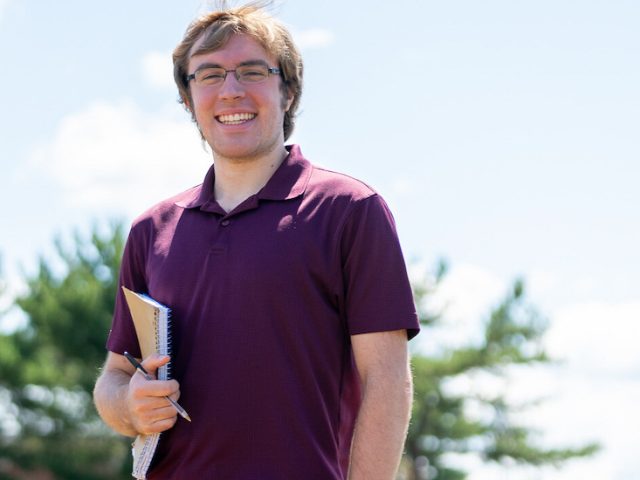 Larry holds a notebook outside on an athletic field.