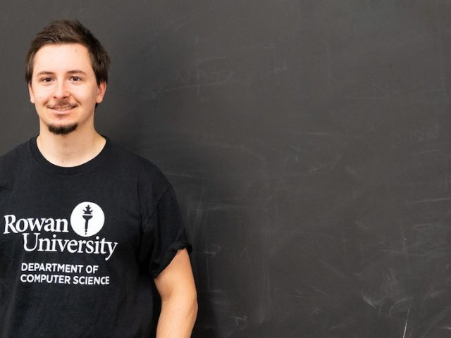 Jon stands in front of a chalkboard inside a a classroom on campus.