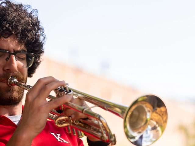 Music education alumnus Mike Massaro plays the trumpet wearing a red polo shirt.