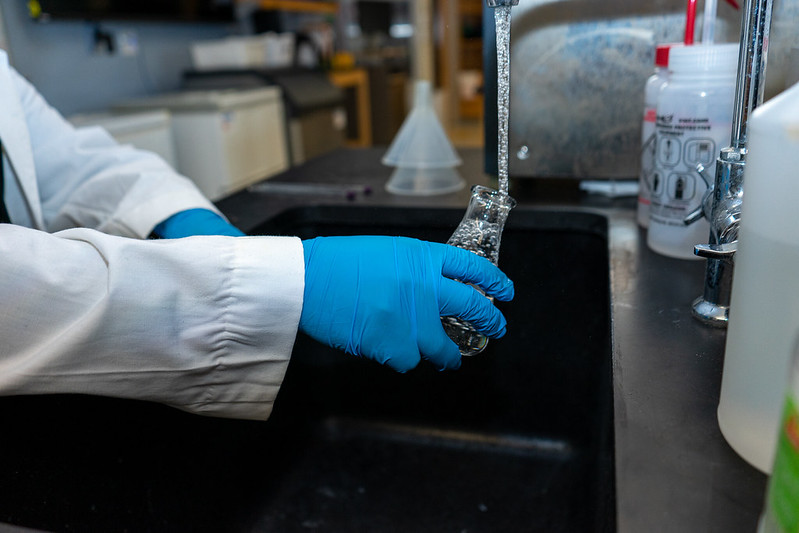 Daniel is pouring water into one of the flasks in the lab. 