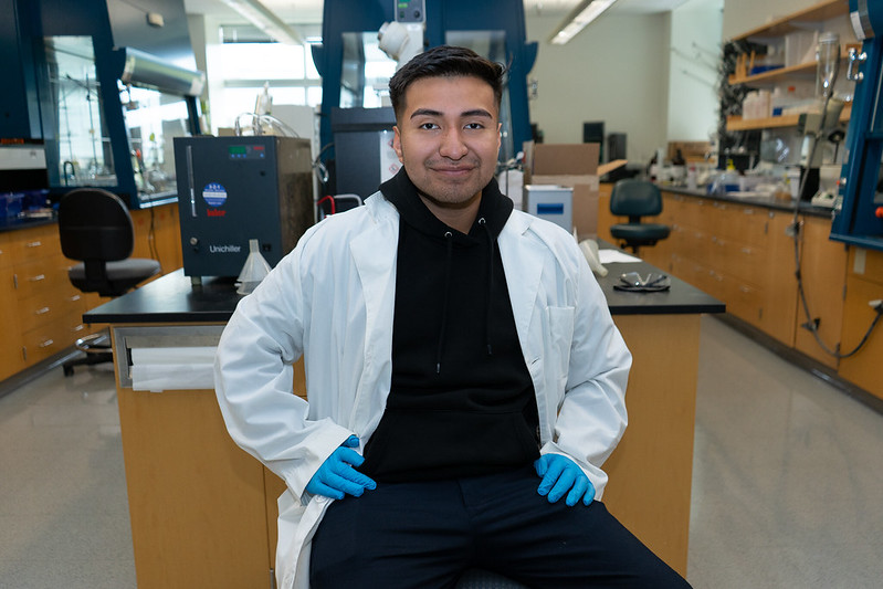 Daniel is sitting directly in front of the camera smiling in the lab.