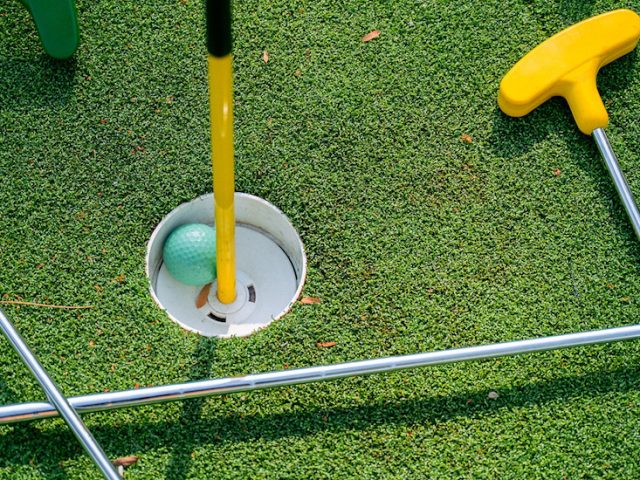 Stock image of mini golf clubs, a ball and course hole.