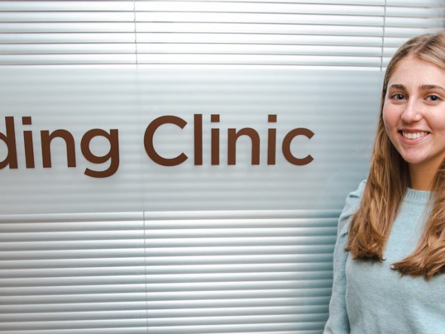 Rowan College of Education student Isabella stands next to the Reading Clinic room inside James Hall.