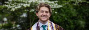 Mark wears his graduation gown for a close up portrait.