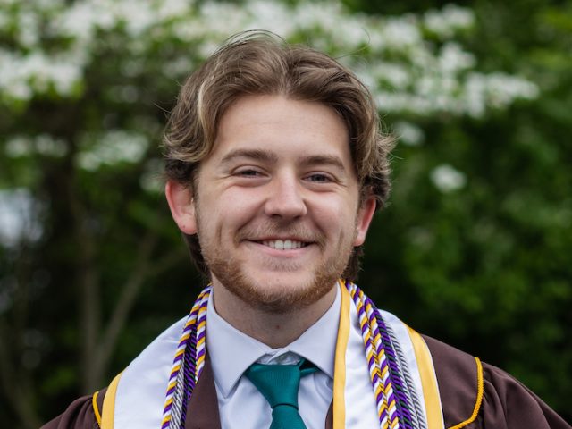 Mark wears his graduation gown for a close up portrait.