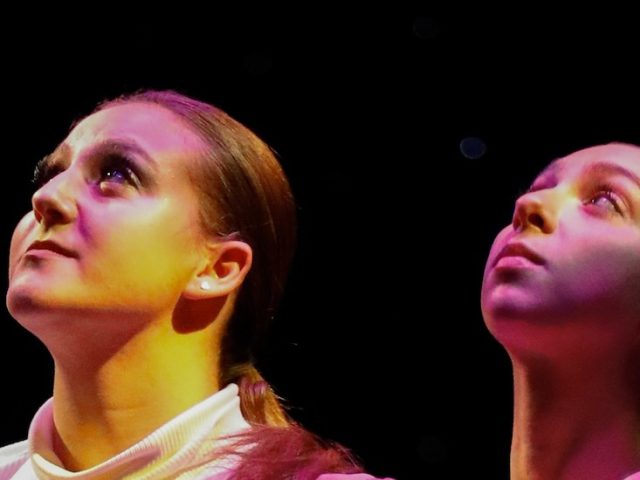 A close up of two dancers faces as they look serious, faces upturned.