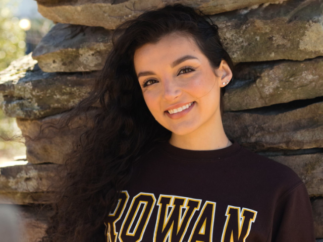 Rowan University Psychology major Siena stands underneath the art installation Time Sweeps by Discovery Hall.