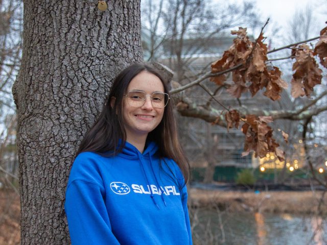 Jade stands in front of a tree, smiling.