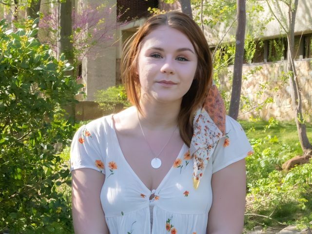 Paige stands in the sun with flowers behind her.