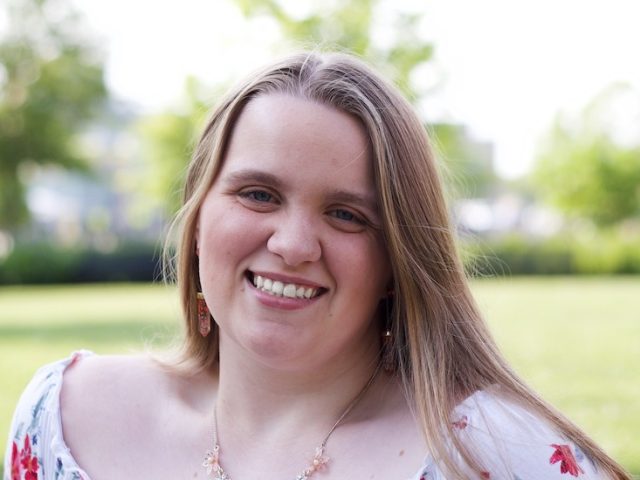 A close up of Heather as she sits smiling at Robinson Circle on Rowan University's campus.