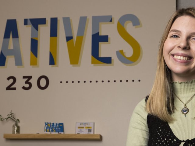 Isabella smiles in front of the Creatives 230 sign