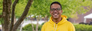 Osvaldo smiles at the camera while outside wearing a bright yellow Rowan shirt.