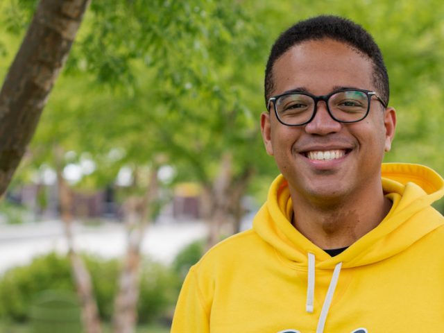 Osvaldo smiles at the camera while outside wearing a bright yellow Rowan shirt.