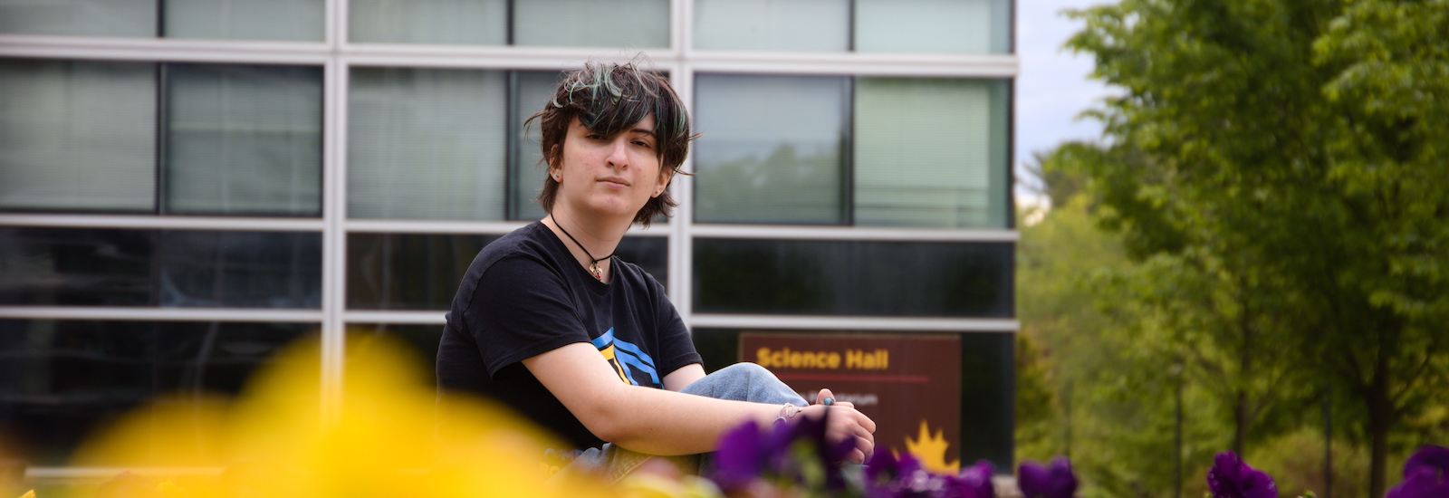 Julie sits in front of Science Hall with yellow flowers in front of her.