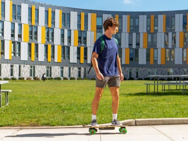 A student riding a skateboard outside Holly Point.