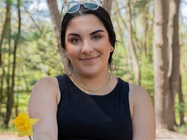 Alexia poses for a portrait surrounded by trees on campus.