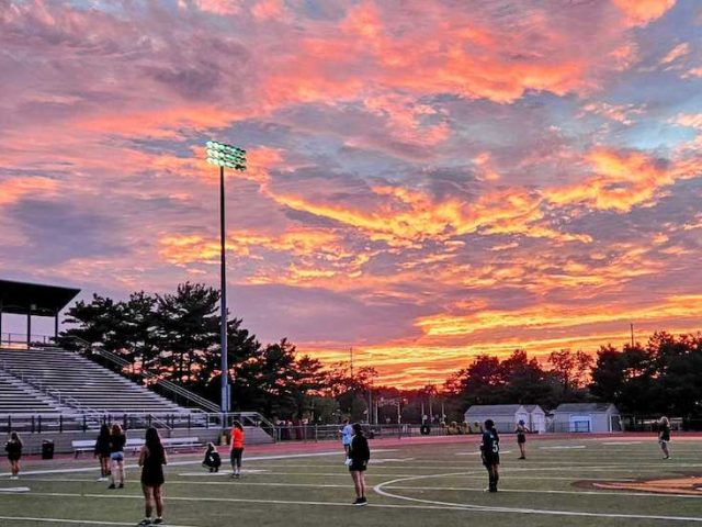 Dramatic sunset photo over the athletic field with the marching band on the field at Rowan University.