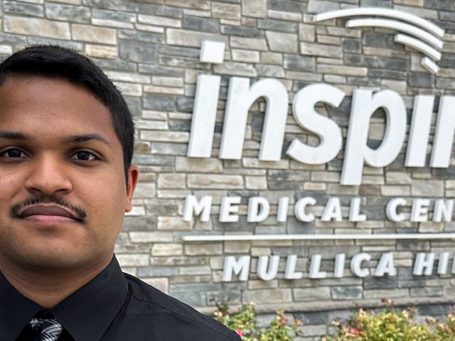 Jonathan stands outside his workplace with the Inspira logo behind him.